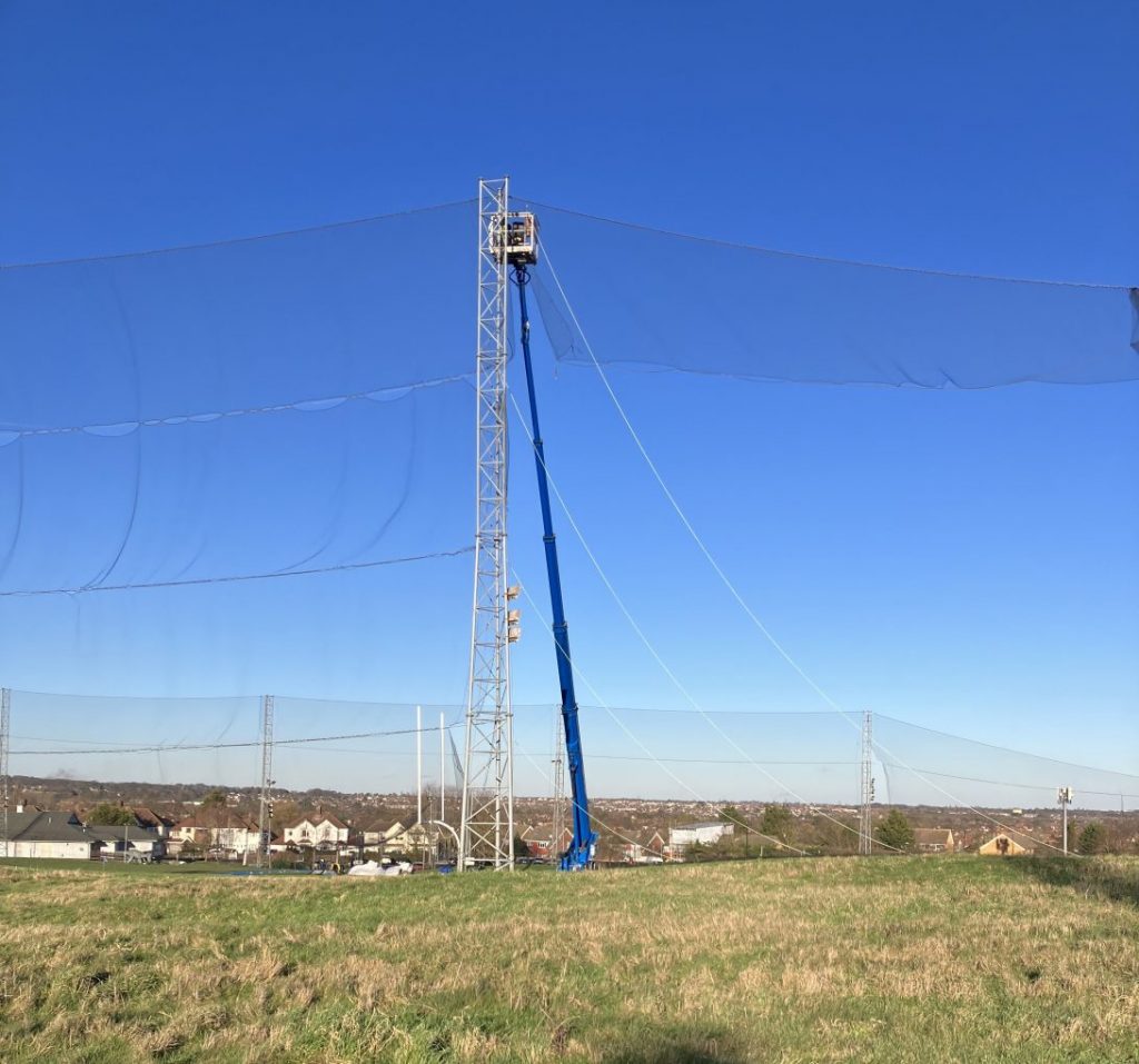 Golf driving range net installation with tall support poles in open field