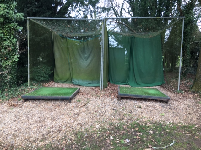 Outdoor golf practice bays with netting in wooded area