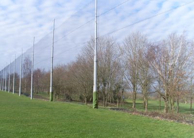 Golf course driving range with tall netting poles and surrounding trees